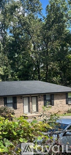 A house with a brown roof and a white door is surrounded by greenery.
