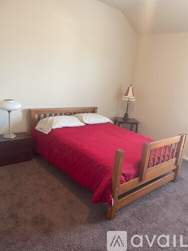 A bed with red bedspread and white pillows is in a room with a carpeted floor.