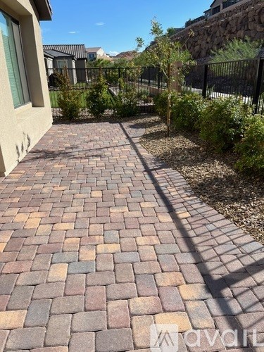 A brick pathway leads to a house with a black fence and green plants.