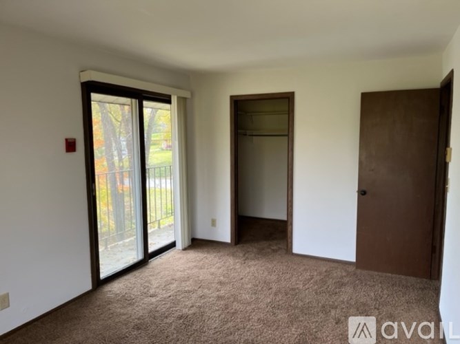 A room with a carpeted floor, a sliding glass door, and a brown door.