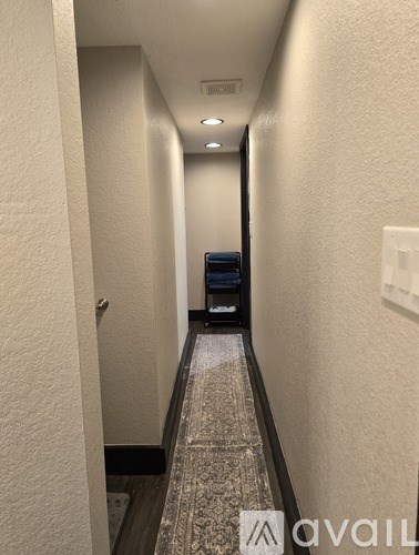 A hallway with a carpeted floor and a light switch on the wall.