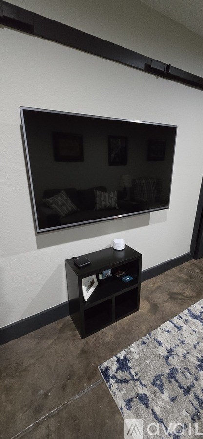 A black TV is mounted on a white wall above a black table.