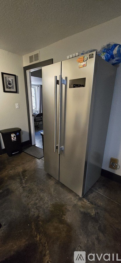 A silver fridge in a room with a black trash bin.