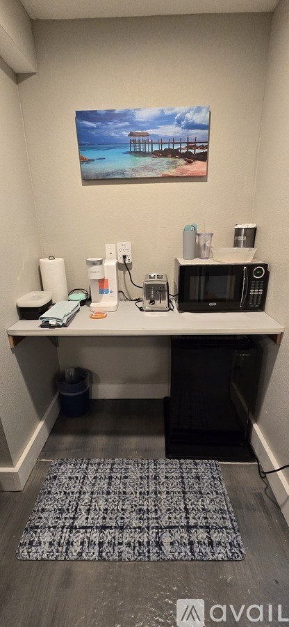 A room with a desk, a fridge, and a painting on the wall.