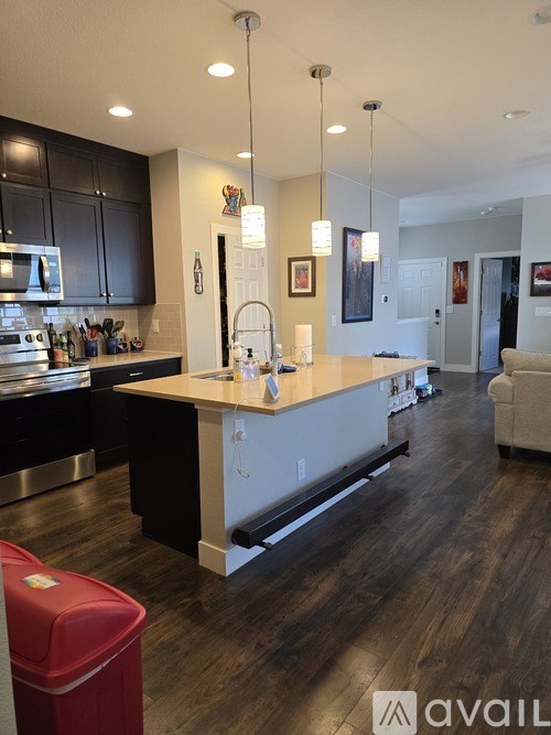 A modern kitchen with dark wood floors and a red trash can.