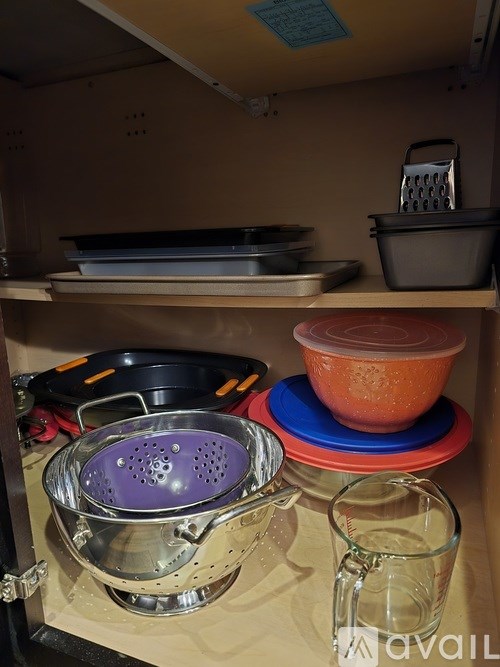 A kitchen cabinet with a colander and a glass mug.