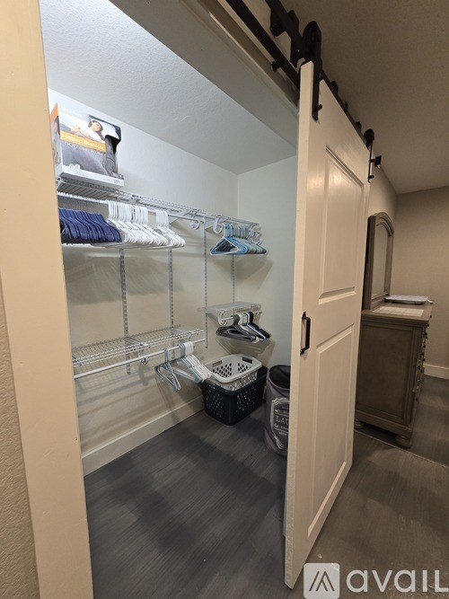 A walk-in closet with clothes hanging on shelves and a trash can on the floor.