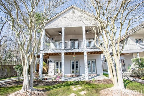 A white house with a porch and trees in front.