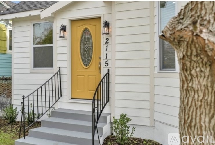 A white house with a yellow door and black railings.