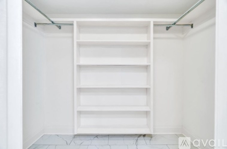 A white shelving unit with five shelves is in a white room.