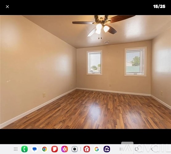 A room with wooden flooring and two windows.