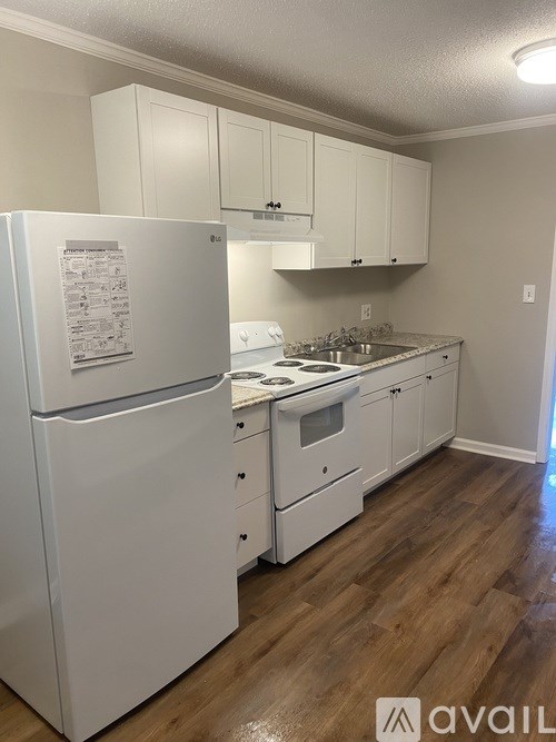 A white fridge in a kitchen with wooden floors and white cabinets.