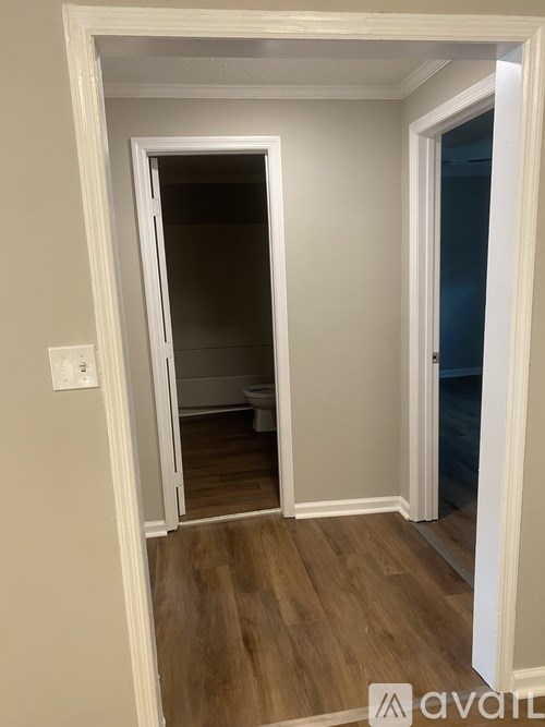 A white doorway opens to a bathroom with a toilet and wooden floors.