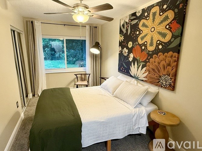 A bedroom with a bed, a ceiling fan, and a large floral picture on the wall.