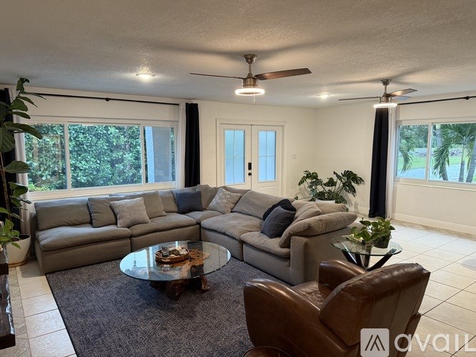 A living room with a grey sofa, a glass coffee table, and a ceiling fan.