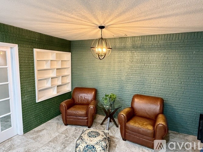 Two brown leather chairs are placed in a room with a green wall and a hanging light fixture.