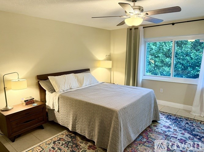A bedroom with a bed, nightstand, and window.