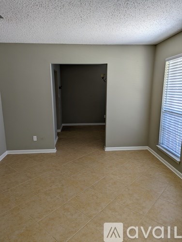 A room with beige walls and floor, a door, and a window with blinds.