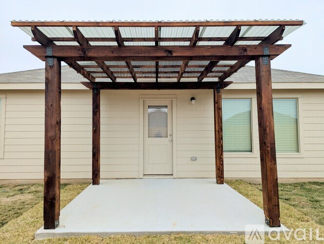 A wooden pergola attached to a house with a white door and windows.