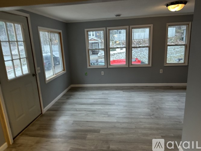 A room with grey walls and wooden flooring with a view of a snowy landscape through the windows.