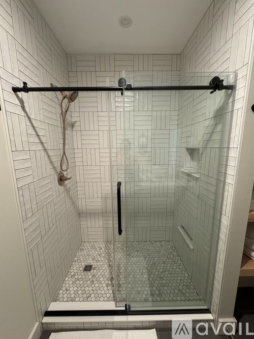 A white tiled shower with a glass door and a black grab bar.