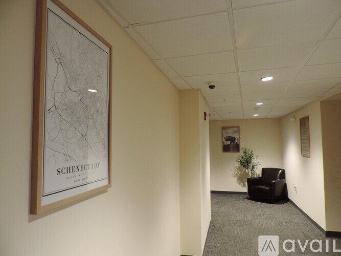 A hallway with a framed map on the wall and a black chair in the corner.