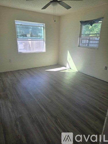 A room with wooden flooring and two windows.