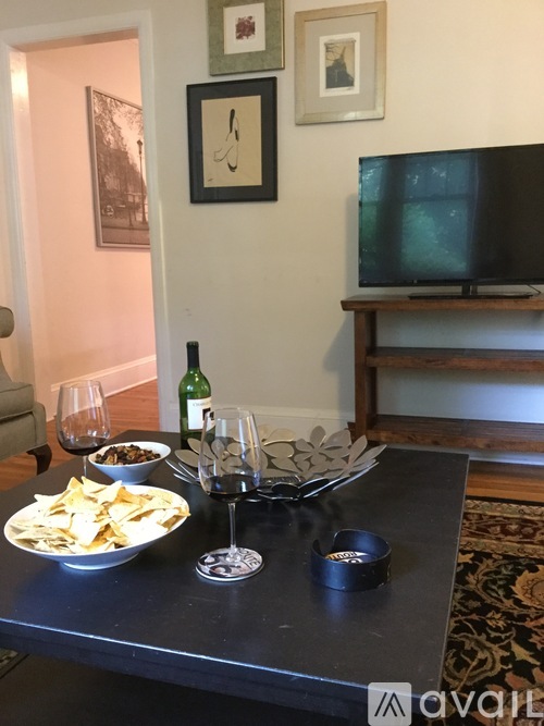 A black table with a bowl of chips, a glass of wine, and a bottle of wine on it.