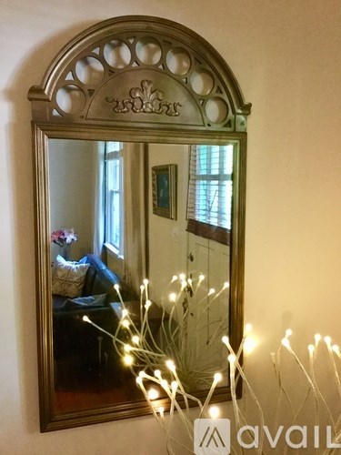 A mirror with a decorative frame reflects a room with a couch and a window.