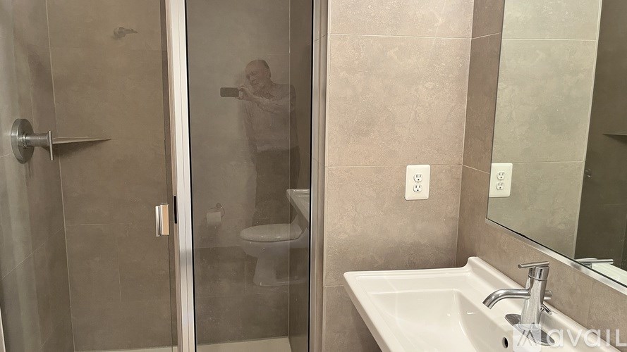 A man is taking a picture in a bathroom with a white sink and a toilet.