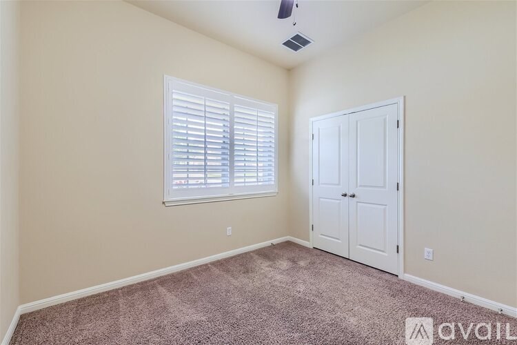 A room with a carpeted floor, a window with blinds, a ceiling fan, and a door.