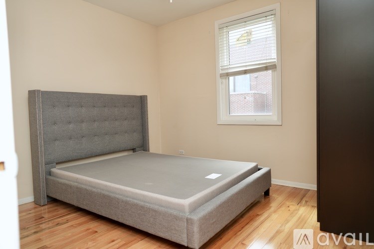 A bed with a grey headboard and a grey mattress is in a room with a window.