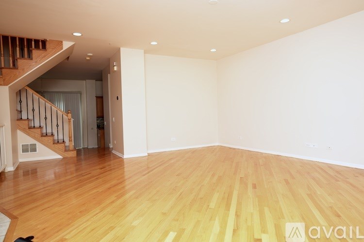 A room with wooden flooring and a staircase in the background.