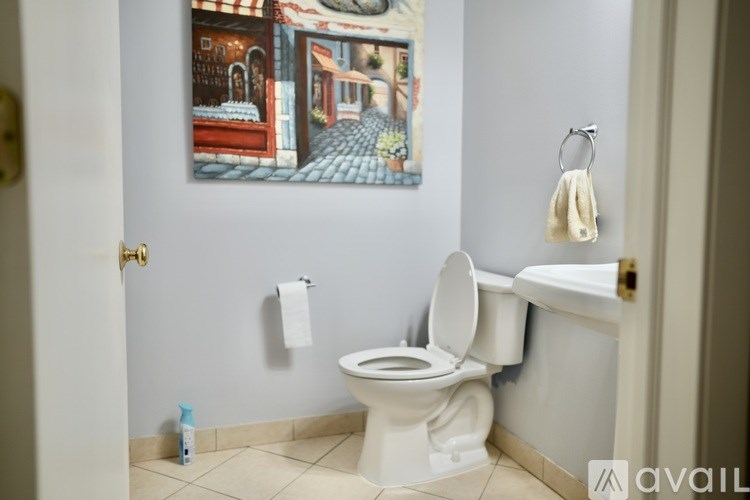 A bathroom with a toilet, a sink, and a painting on the wall.