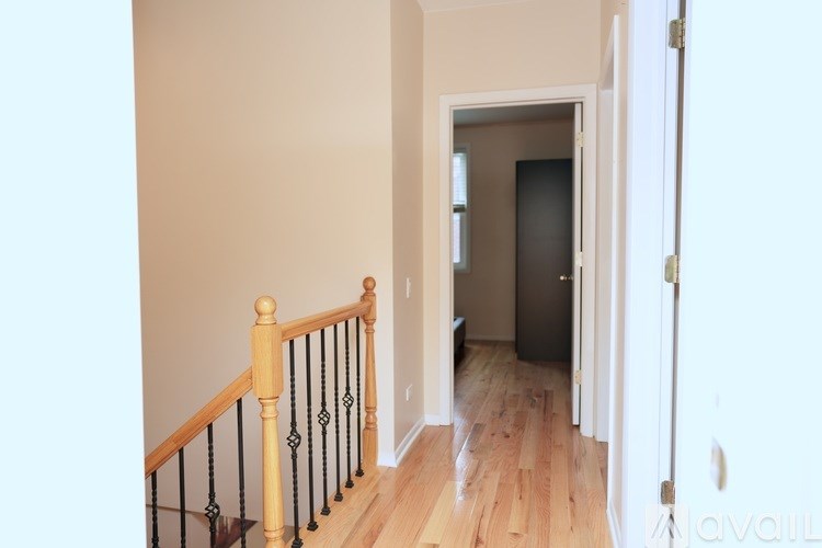 A hallway with a wooden floor and a staircase with a black railing.