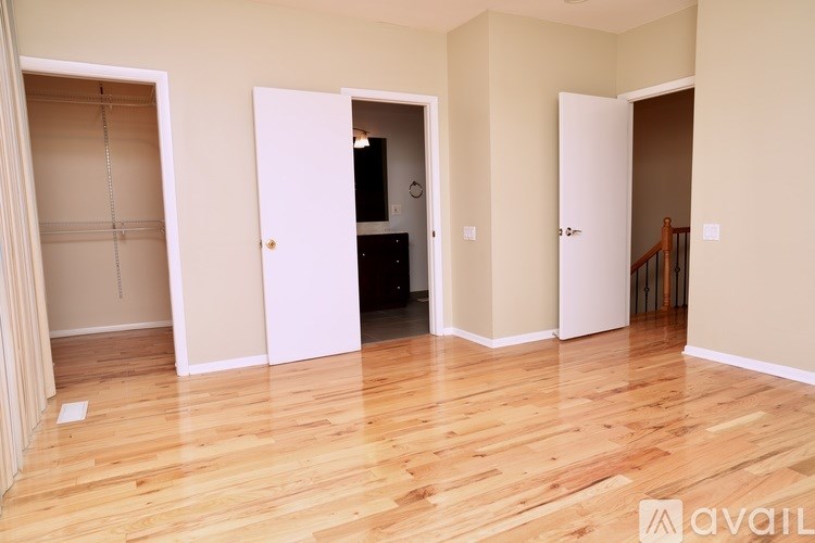 A room with wooden flooring and three doors, one of which is open.