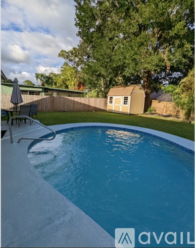 A pool with a chair and umbrella in the foreground and a house in the background.