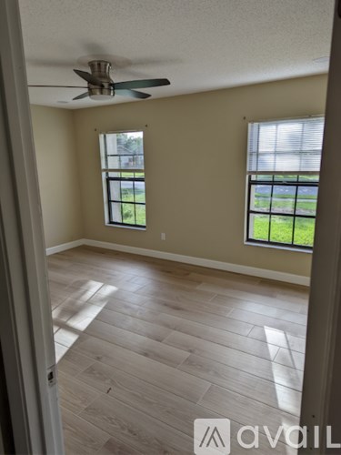 A room with a ceiling fan and two windows.