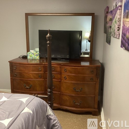 A wooden dresser with a mirror and a television on top of it.