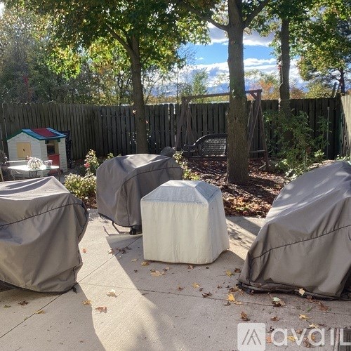 A patio with a small house, a bench, and a table covered in a grey cloth.