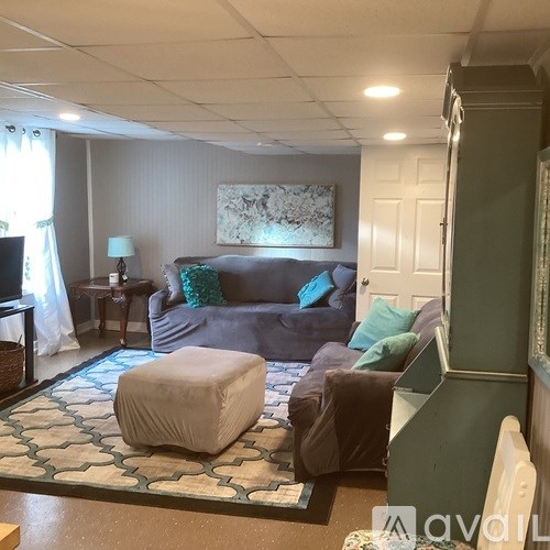 A living room with a grey couch, a white ottoman, and a green cabinet.