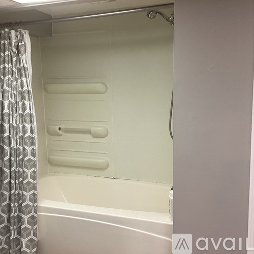 A white bathtub with a shower head and a grey and white shower curtain.