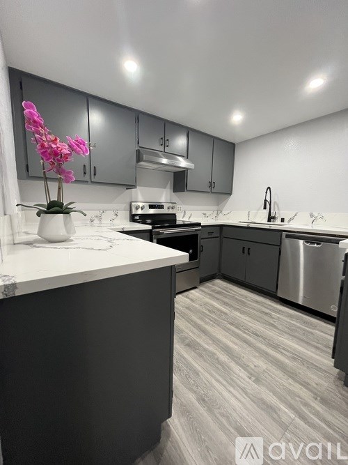A kitchen with a white counter top and a vase of pink flowers.
