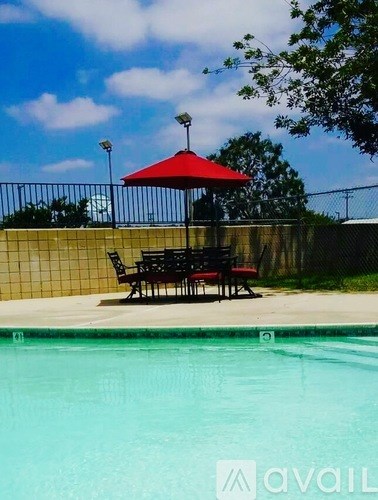 A pool with a red umbrella and a black bench.
