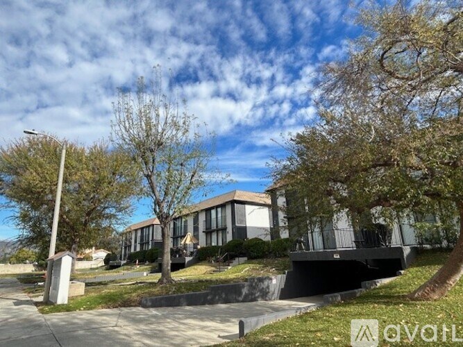 A modern building with a flat roof and large windows is surrounded by trees and a well-maintained lawn.