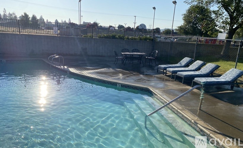 A pool with sunlight reflecting on the water and chairs on the side.