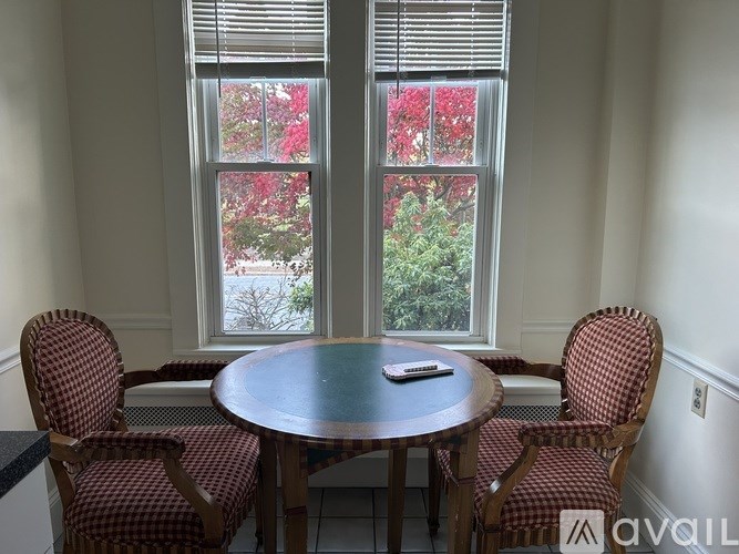 A table with chairs in front of a window with red flowers.