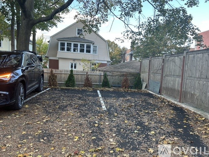 A car is parked in a driveway with a house and fence in the background.