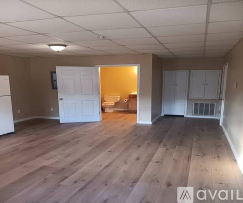 A room with wooden floors and white walls, with a white refrigerator and cabinets.