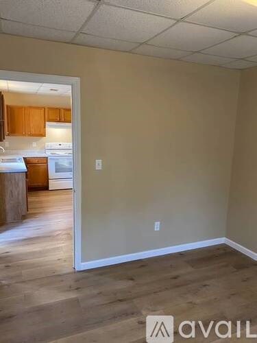 A room with beige walls and wooden flooring with a doorway leading to a kitchen.